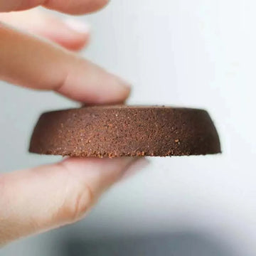 Un'immagine che mostra una persona che tiene in mano un disco di fondi di caffè usati, ottimo per riutilizzo.
